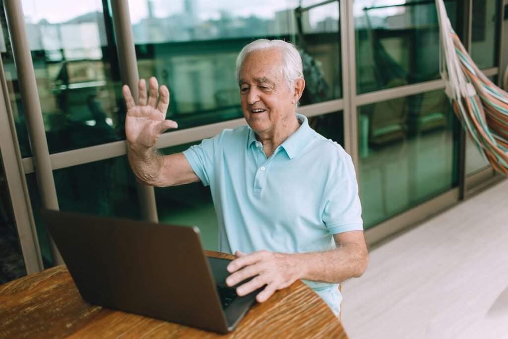 "Idoso sorrindo enquanto usa um tablet para conversar com alguém, simbolizando conexão e inclusão digital."